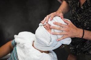 le coiffeur couvre le visage d'un homme avec une serviette chaude. rituel traditionnel de rasage de la barbe avec des compresses chaudes et froides dans un salon de coiffure à l'ancienne. photo