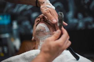 rasoir dans les mains d'un coiffeur spécialisé. coiffeur rasant un homme dans un salon de coiffure, gros plan. homme mith moustaches ayant un rasage photo