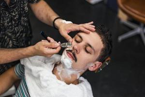 rasoir dans les mains d'un coiffeur spécialisé. coiffeur rasant un homme dans un salon de coiffure, gros plan. homme mith moustaches ayant un rasage photo