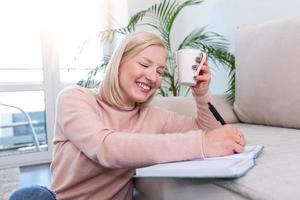 jeune femme étudiant et buvant du café, jeune femme studieuse travaillant à la maison assise sur le sol dans le salon avec des notes de classe dans des classeurs étudiant pour l'université photo