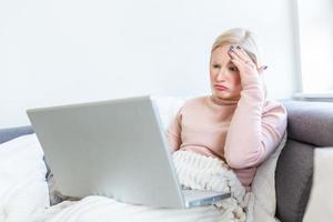 se sentir épuisé. jeune femme frustrée qui a l'air épuisée alors qu'elle est assise sur son lieu de travail à la maison. freelance surmené ayant mal à la tête photo