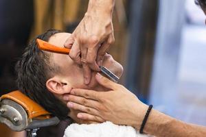 rasoir dans les mains d'un coiffeur spécialisé. coiffeur rasant un homme dans un salon de coiffure, gros plan. homme mith moustaches ayant un rasage photo