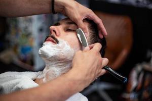 rasoir dans les mains d'un coiffeur spécialisé. coiffeur rasant un homme dans un salon de coiffure, gros plan. homme mith moustaches ayant un rasage photo