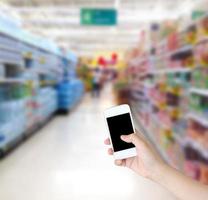 main tenant un smartphone avec des étagères d'eau dans un arrière-plan flou de supermarché photo