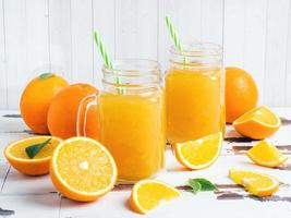 jus d'orange dans des bocaux en verre et des oranges fraîches sur un fond rustique en bois blanc. photo