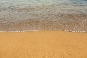 fond avec du sable doré sur la côte de l'île de crète. surface abstraite avec du sable et de l'eau de mer claire pour le texte. photo