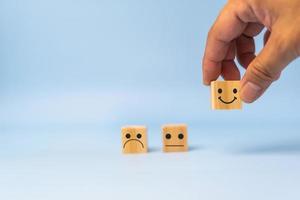 service à la clientèle et concept de satisfaction icône de visage souriant heureux. commentaires d'affaires note positive cube de bois très impressionné sur la table. photo