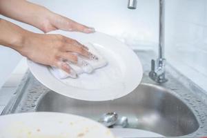 gros plan sur une femme asiatique lave le plat dans la cuisine avec son éponge à vaisselle. photo