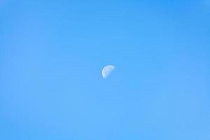 moitié de lune dans le ciel bleu clair du matin photo