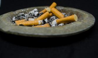 vue à plat des mégots de cigarettes sales dans le cendrier sur fond noir photo