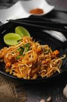 pad thai ou fried noodle thai style, style thai servi avec citron vert et assaisonnements. dans une palette noire, le style visuel est des tons sombres.