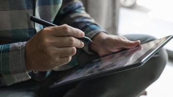 les concepteurs choisissent des pièces de décoration pour la maison sur une tablette, un graphiste travaille sur la conception d'un stylo sur une tablette, un homme tenant un stylo et une tablette assis par terre dans la maison. photo