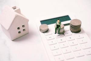 figurine de gens d'affaires miniature assis sur une pile de pièces de monnaie sur une calculatrice avec un concept de maison, financier et immobilier photo