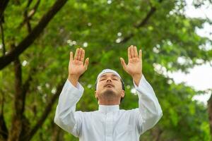 homme musulman asiatique priant les bras levés avec fond de forêt photo