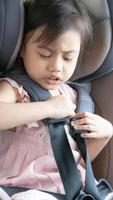 portrait dramatique d'une jolie petite fille asiatique de 4 ans, petite enfant d'âge préscolaire attachée avec des ceintures de sécurité, assise dans un siège enfant dans la voiture. enfant essaie de déboucler la ceinture de sécurité de la voiture photo