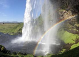 un arc-en-ciel devant la cascade de seljalandsfoss sur la côte sud de l'islande lors d'une journée ensoleillée photo