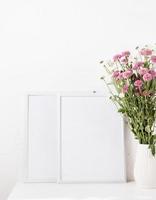 maquette de cadre blanc avec des fleurs de chrysanthème dans un vase sur un tableau blanc photo