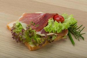 sandwich au prosciutto sur planche de bois et fond en bois photo