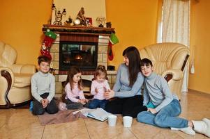 heureuse jeune famille nombreuse près d'une cheminée dans un salon chaleureux le jour de l'hiver. mère avec quatre enfants à la maison. photo