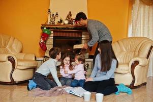 heureuse jeune famille nombreuse à la maison près d'une cheminée dans un salon chaleureux le jour de l'hiver. photo