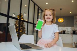 petit enfant assis au bureau avec un ordinateur portable tenir un téléphone portable photo
