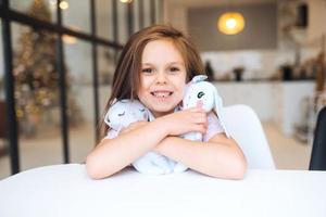 petite fille souriante étreignant ses jouets préférés assis à table photo