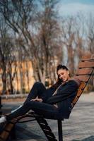 jeune femme assise sur un banc dans le parc, souriant et regardant la caméra photo