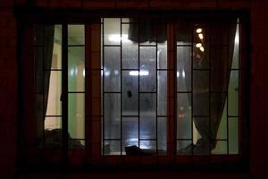 la fenêtre est dans le noir. lumière de la fenêtre en ville. grille sur le bâtiment la nuit. photo