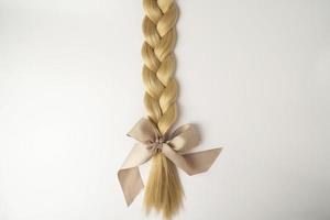 une tresse blonde avec un arc beige allongé sur un fond blanc photo