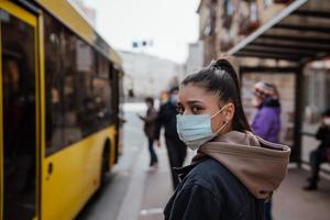 jeune femme portant un masque chirurgical en plein air à l'arrêt de bus dans la rue photo