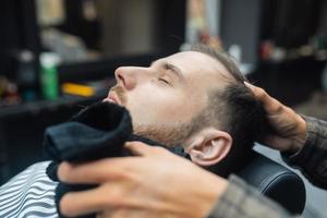 Barber prépare le visage de l'homme pour le rasage avec une serviette chaude dans un salon de coiffure photo