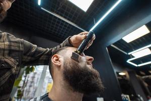 barbier travaille avec une tondeuse à barbe. client hipster se coupe les cheveux. photo