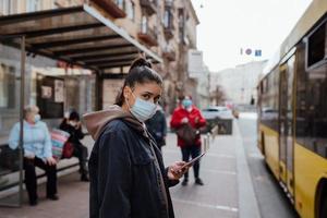 jeune femme portant un masque chirurgical en plein air à l'arrêt de bus dans la rue photo