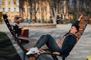 jeune femme assise sur un banc dans le parc, souriant et regardant la caméra photo