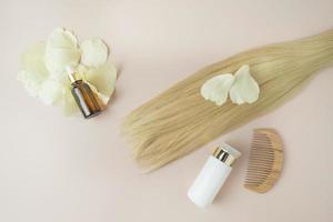 une mèche de cheveux blonds, un flacon compte-gouttes d'huile essentielle naturelle pour le traitement des cheveux et un peigne en bois photo