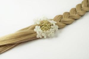 Une tresse de cheveux blonds avec une fleur blanche dessus allongé sur un fond blanc photo