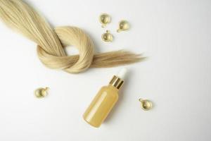 cheveux blonds naturels et huile essentielle pour le traitement des cheveux dans des capsules dorées sur fond blanc photo