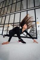 jeune femme portant un costume de sport noir exerçant une pose de yoga à l'intérieur. photo