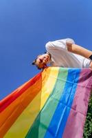 une jeune femme développe un drapeau arc-en-ciel contre le ciel photo