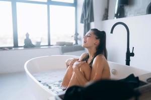 jeune femme étreint ses jambes alors qu'il était assis dans le bain photo