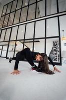 jeune femme portant un costume de sport noir exerçant une pose de yoga à l'intérieur. photo