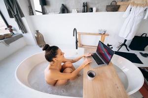 jeune femme travaillant sur un ordinateur portable tout en prenant une baignoire photo