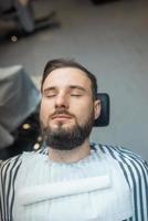 bel homme avec une barbe et les yeux fermés dans le salon de coiffure. photo