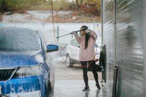 jeune femme lavant une voiture bleue au lave-auto photo