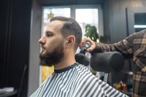 barbier travaille avec une tondeuse à barbe. client hipster se coupe les cheveux.