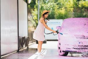 brunette d'un tuyau à haute pression applique un nettoyant sur la voiture photo