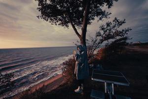 jeune femme prend des photos du coucher de soleil sur la mer par smartphone