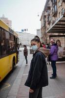 jeune femme portant un masque chirurgical en plein air à l'arrêt de bus dans la rue photo