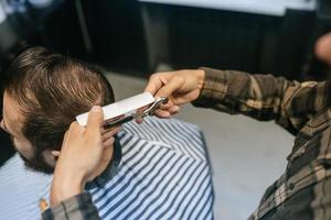 joyeux jeune homme barbu se coupe les cheveux par un coiffeur au salon de coiffure photo