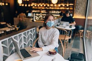 jolie femme portant un masque médical, utilisant un ordinateur portable pour travailler. photo